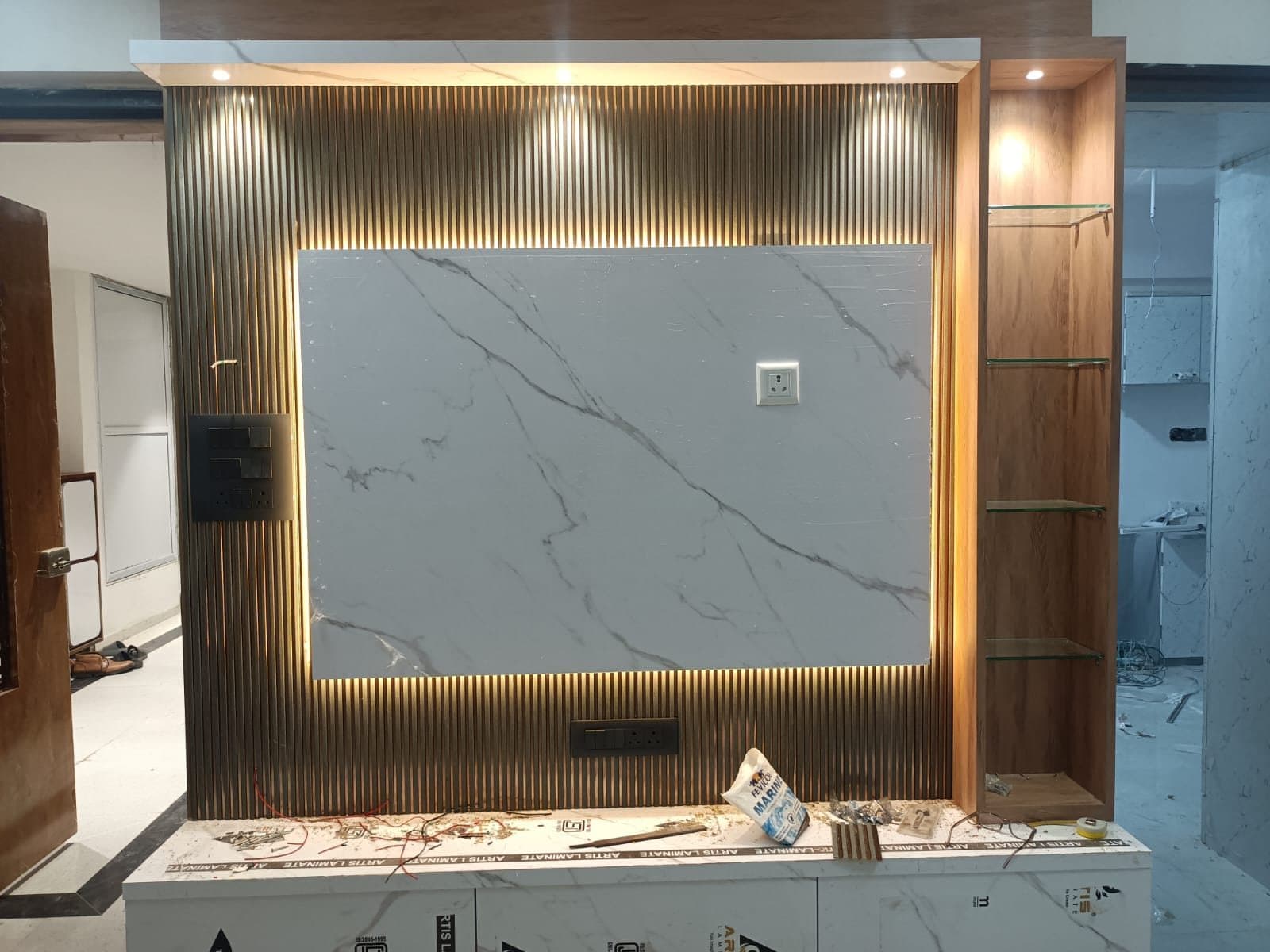 Backlit marble TV feature wall with fluted steel panelling and glass display shelves